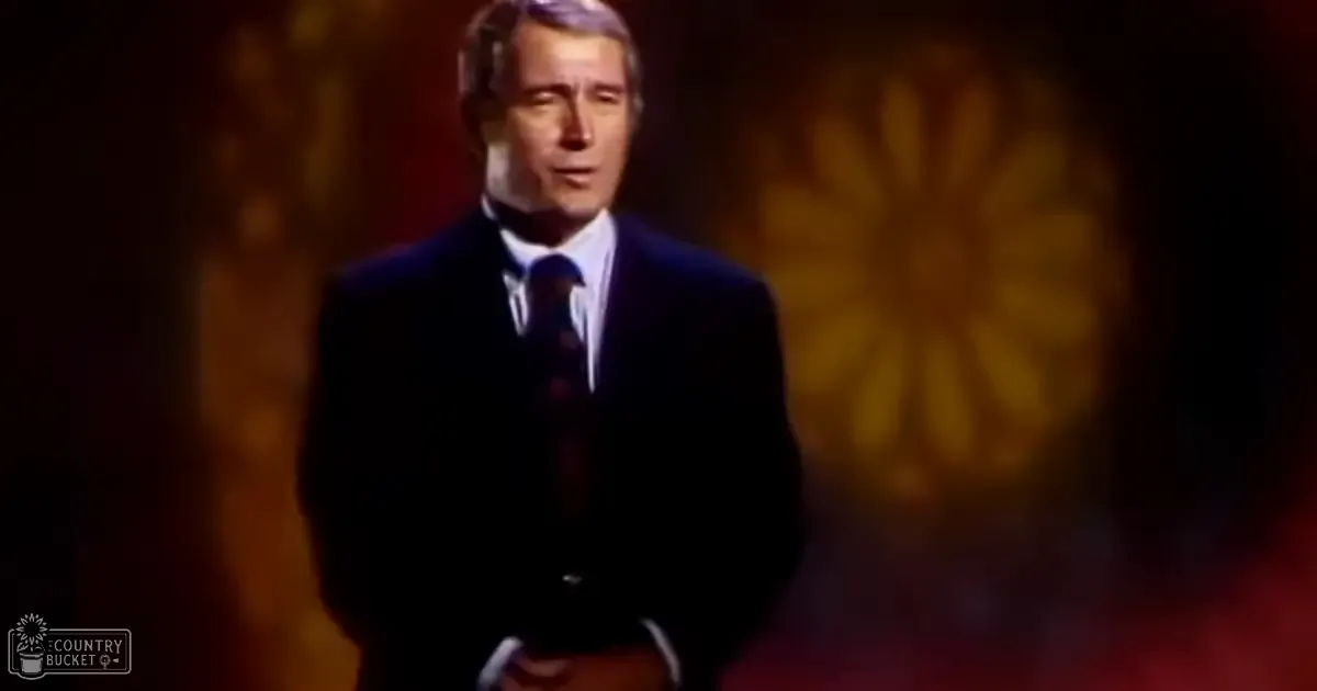 A middle-aged man in a dark suit and white dress shirt, wearing a dark tie with 'Madly Odd' text on the bottom left corner of an indoor setting.