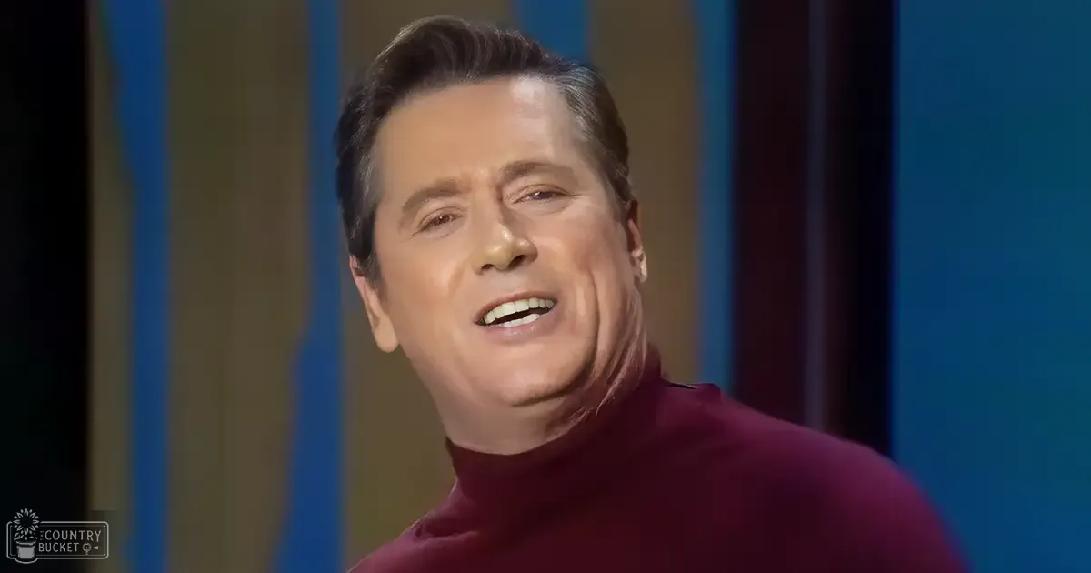 Middle-aged man with short dark hair in a studio setting, wearing a snug maroon turtleneck sweater against a vertical striped background.