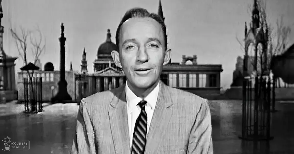 A middle-aged man in a formal suit stands against an indoor backdrop with classical architectural elements, possibly part of a historical or news segment from the mid-20th century.