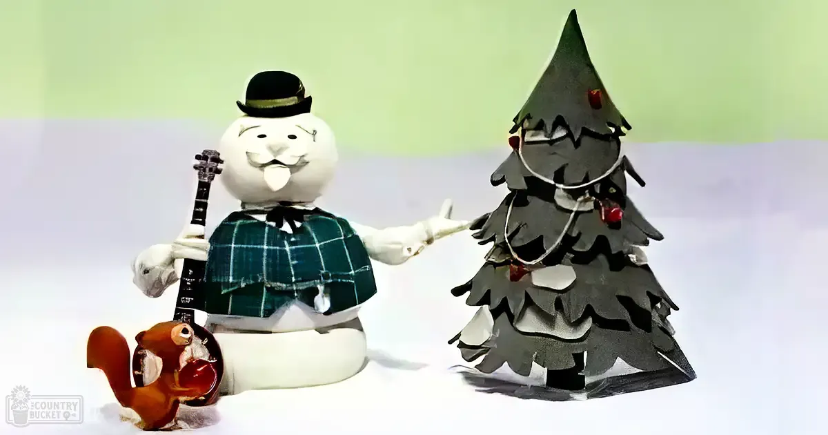 A squirrel with brown fur stands near a festive snowman dressed as a musician, surrounded by a decorated Christmas tree on an indoor light-colored surface.