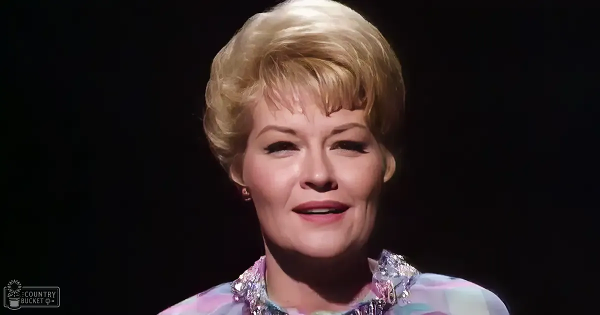 A middle-aged adult female in a fitted, light purple polka dot blouse with decorative embellishments and small earrings, set against a dark background with 'Madly Odd' text faintly visible.
