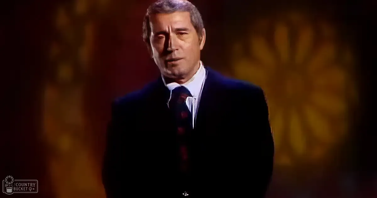 Middle-aged to older adult male wearing a dark suit jacket and white dress shirt at an indoor setting with warm lighting.