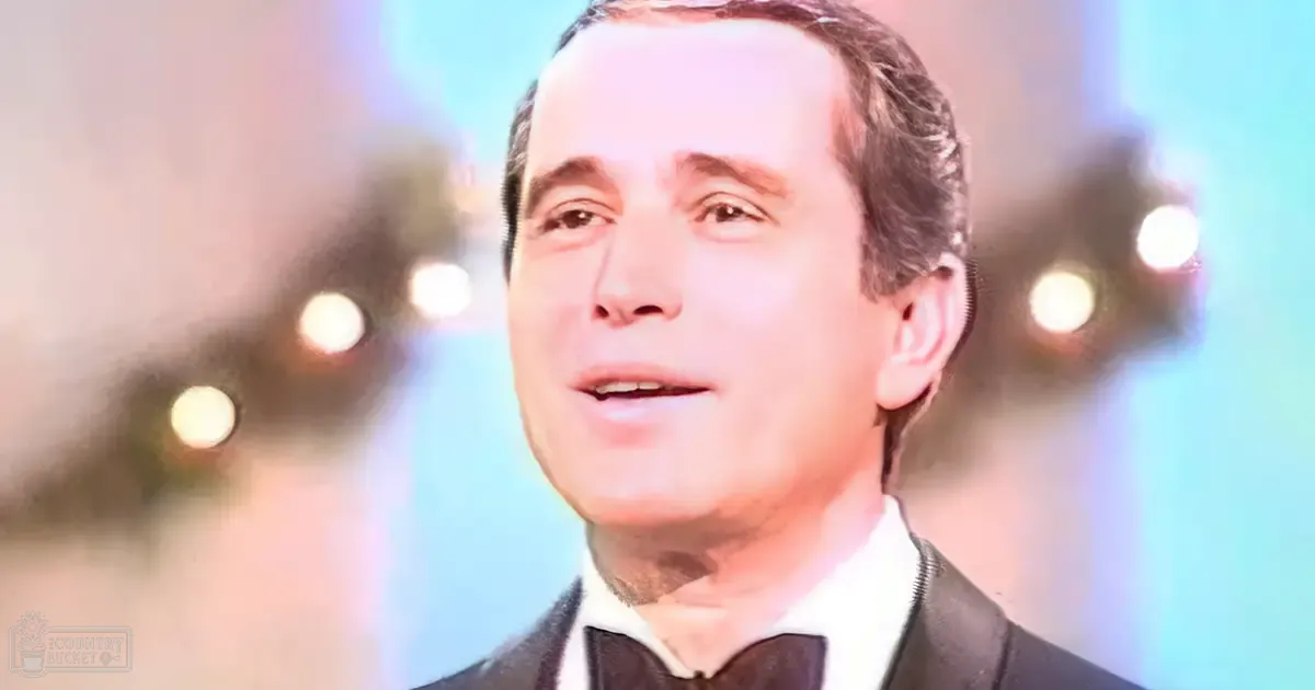 Middle-aged adult male in a formal suit jacket, white dress shirt, and black bow tie at an indoor event with blurred background lights suggesting a festive atmosphere.