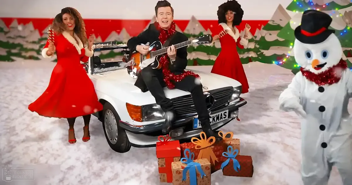 A festive Christmas-themed scene with a white car and wrapped presents on its front bumper, set against a backdrop of snow-covered trees and red-and-white color scheme.