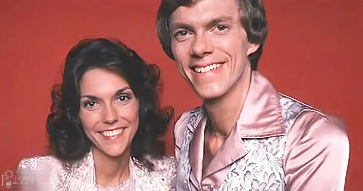 A young adult female and an adult male in an indoor setting, both wearing patterned tops with high necklines and fitted sleeves; the background is a solid red color.