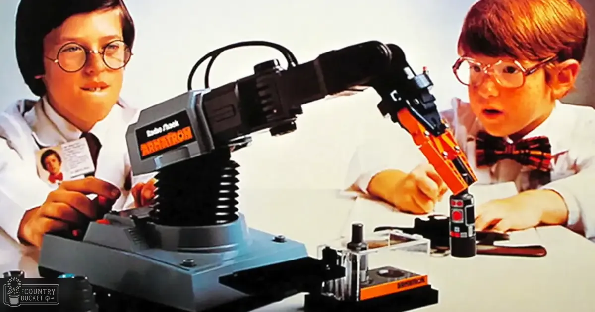 A child wearing a white lab coat with a name tag stands beside another child in the same attire, both interacting with an ARRATRON robotic arm toy on display in what looks like a store or classroom setting.