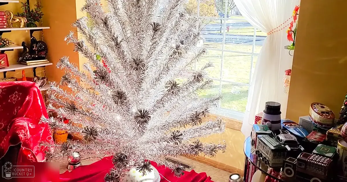 Indoor living room scene with a vintage silver Christmas tree, red floral-patterned chair, greenery outside window, spring or summer light.