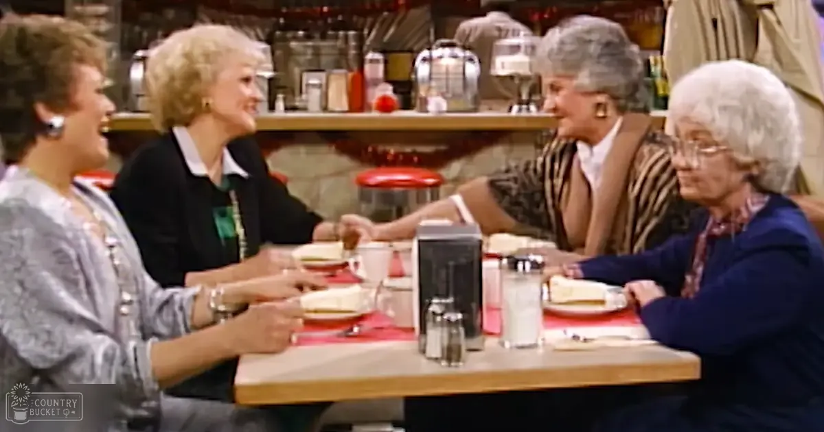 An older adult female group seated at a diner table, dressed in various casual outfits with accessories like earrings and watches, surrounded by red-placemat tables and diner-style decor.