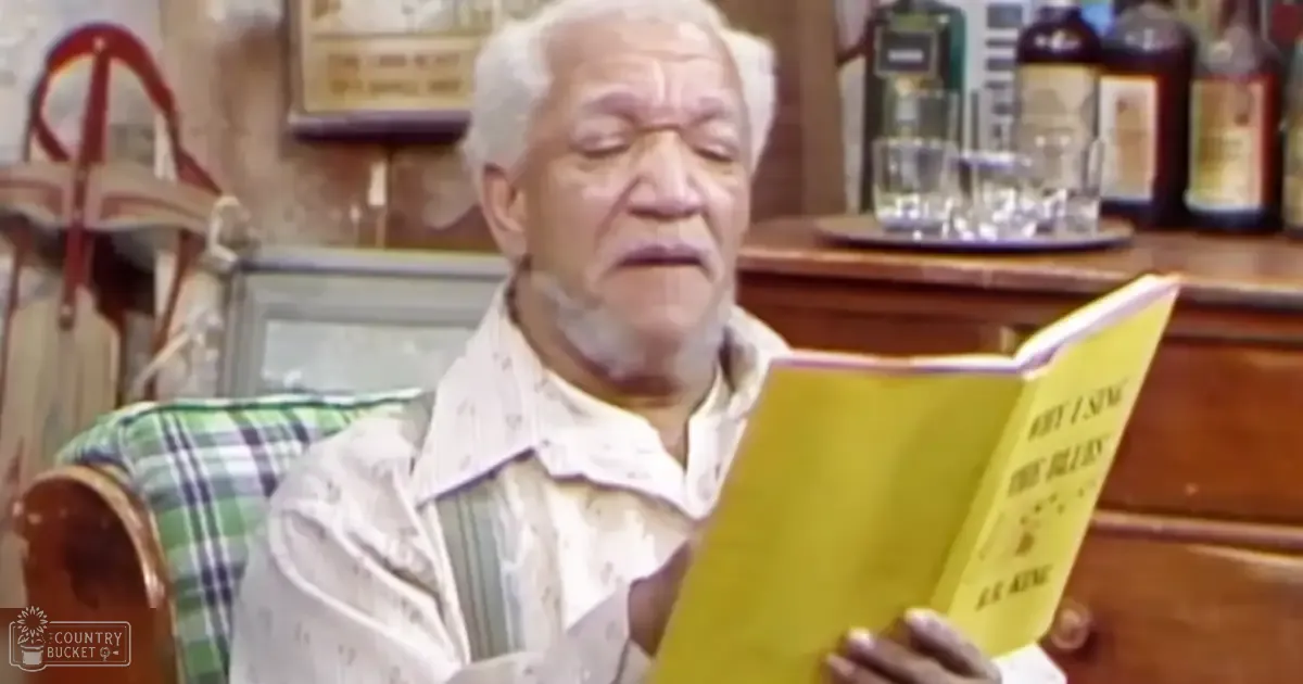 An older adult male wearing a white patterned shirt reads 'If I Sing the Blues' by R.K. Kent in a bar setting with wooden furniture and bottles of alcohol, natural daylight illuminating his face.