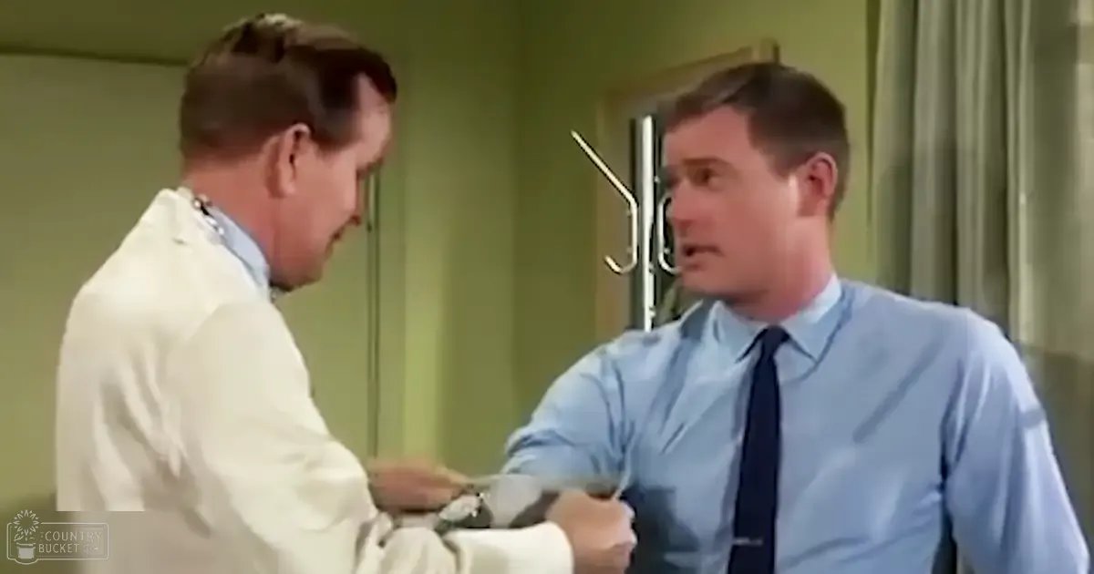 Two adult males in a professional setting, one wearing a lab coat and the other in a dress shirt with tie, against green walls under artificial light.