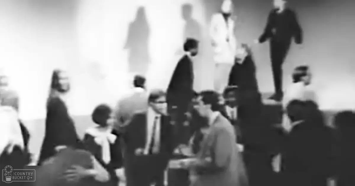 A gathering of adults and children indoors with muted colors and even lighting.