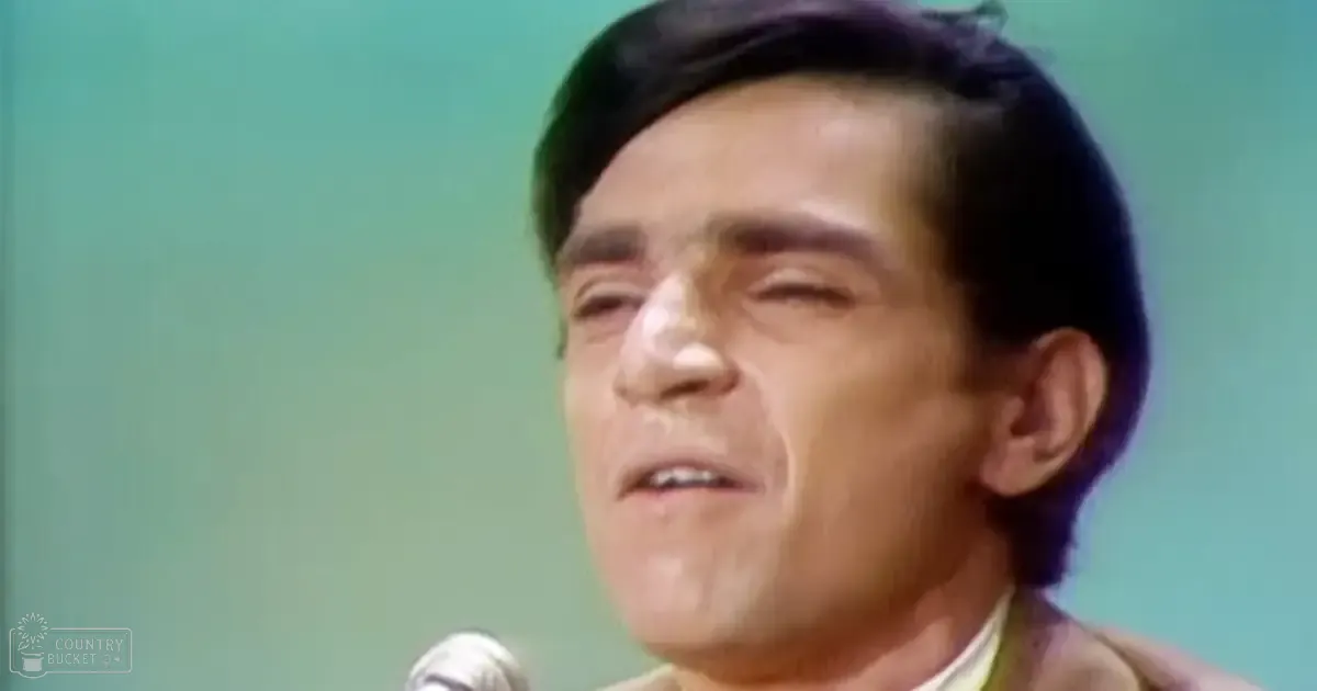 A middle-aged adult male wearing a light-colored collared shirt over a patterned jacket, standing in an indoor setting with artificial lighting.