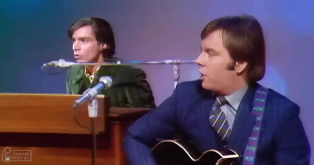 A musical performance scene with young adult males in a stage setting, with a microphone stand and wooden keyboard.