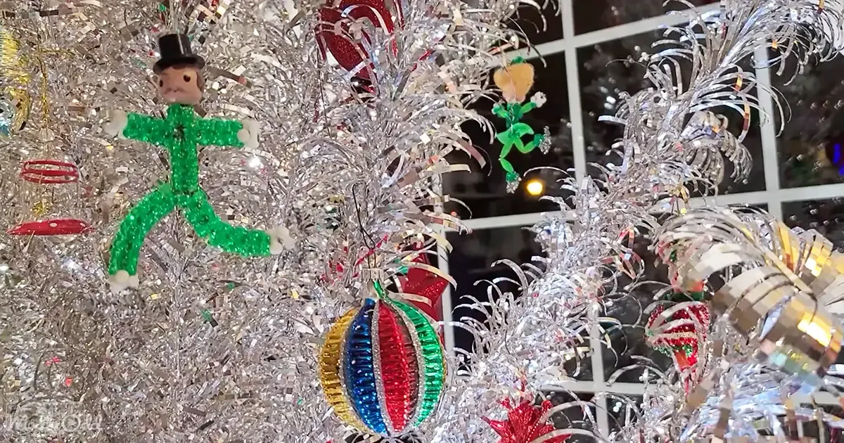 Indoor Christmas tree decorated with colorful ornaments and small figurines in a festive setting.