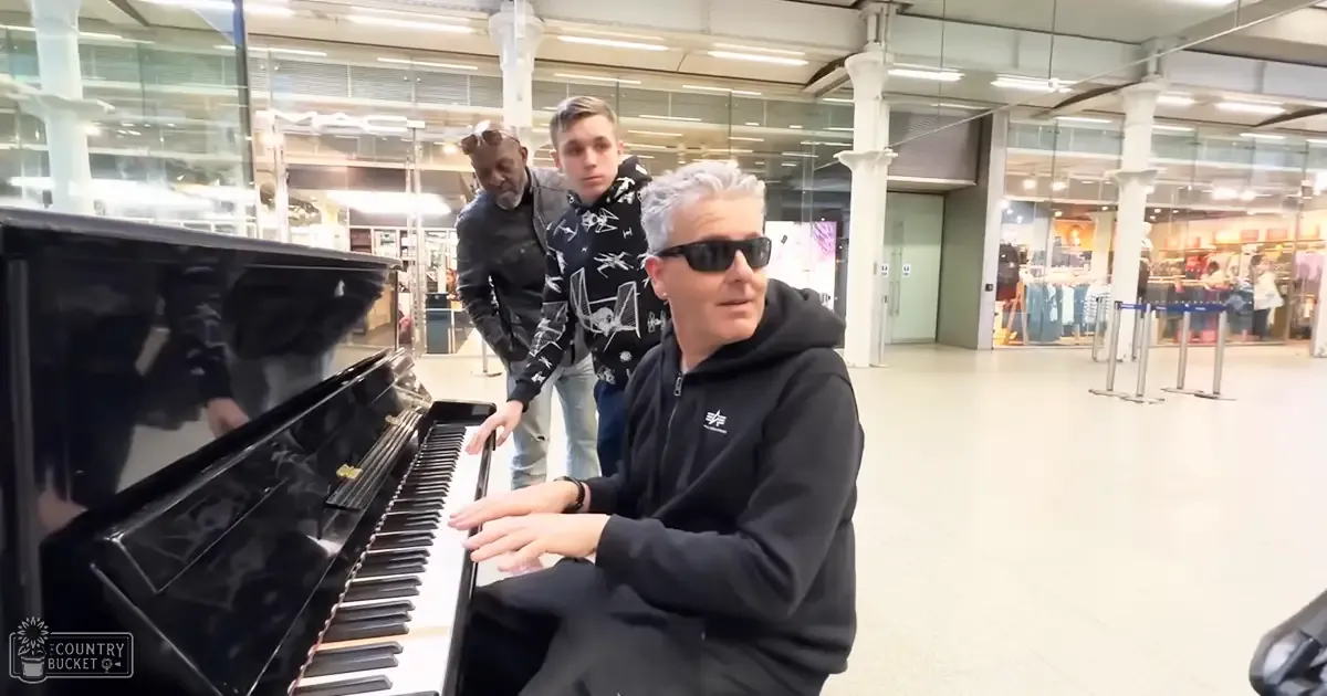 Adult male playing piano in an airport terminal with a teenage boy behind him.