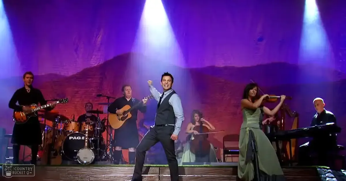 Performers on stage with musical instruments in an indoor venue, stylized rock formations backdrop under purple lighting.