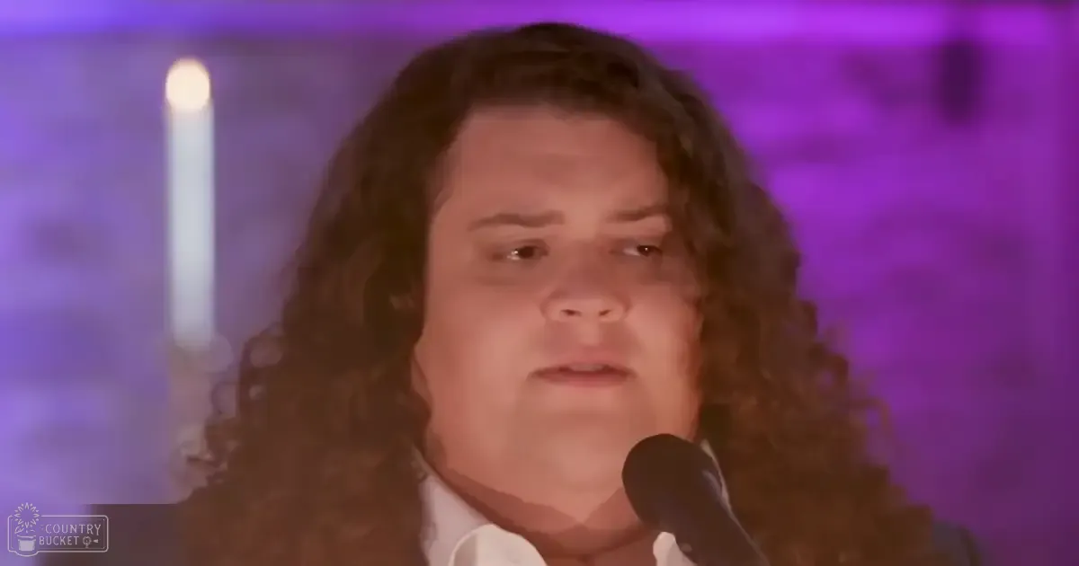 A young adult male with long curly hair stands indoors, wearing a modern casual white collared shirt with long sleeves and a cotton blend material.