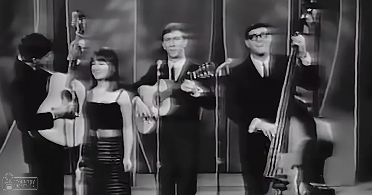 A black and white image capturing a live musical performance with multiple musicians on stage, dark curtains suggesting an indoor venue from the mid-20th century.