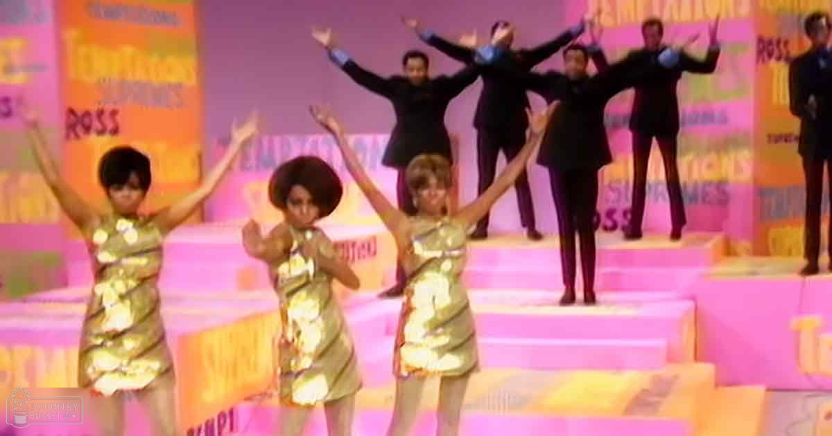 Children in gold sequined dresses perform on stage with adults in dark suits, vibrant backdrop with 'Tourettes' and 'Ross,' suggesting a 1960s musical or variety show setting.
