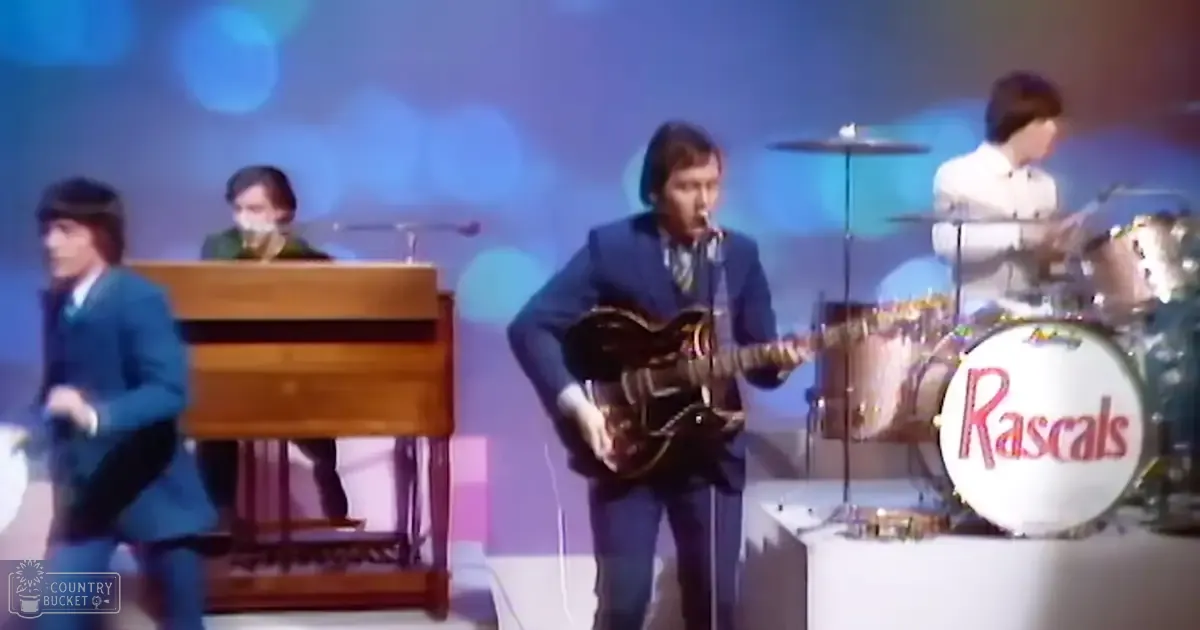 A musical performance from the 1960s or early 1970s, with a young adult male singer and musicians on stage with a colorful backdrop.