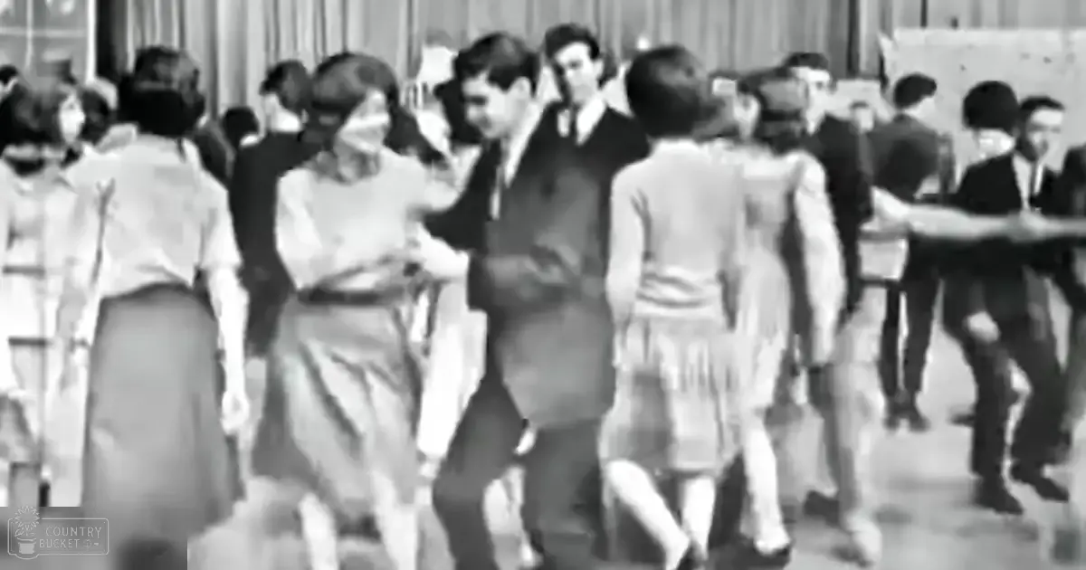 A group dance scene from the mid-20th century in an indoor setting like a school gymnasium.
