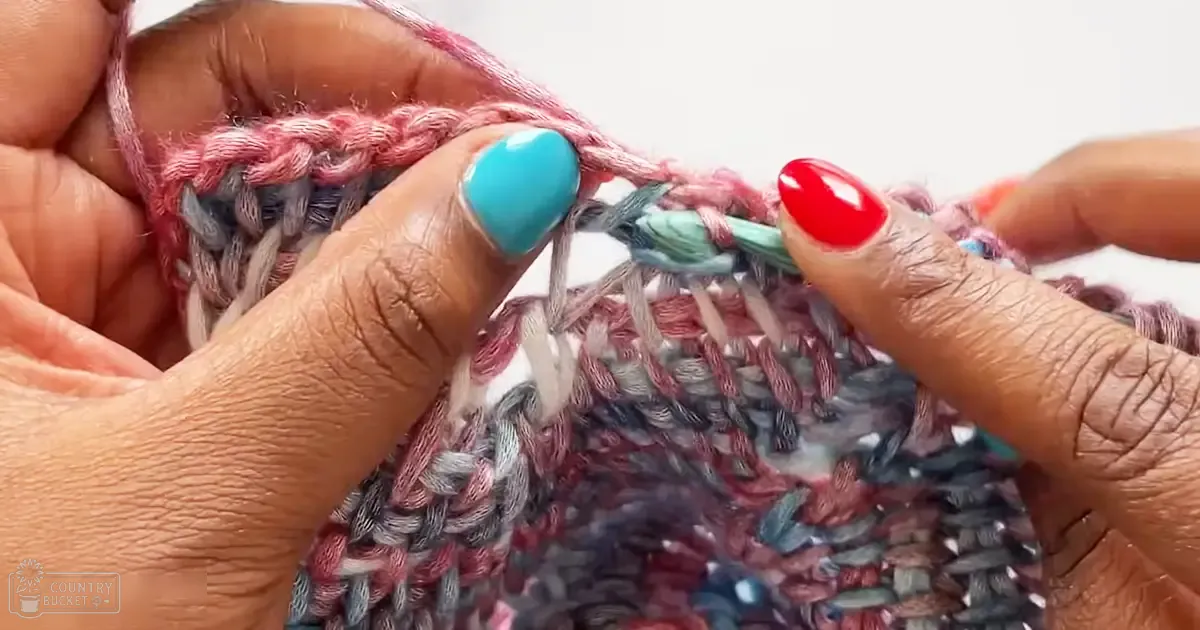Close-up of hands engaged in knitting or crocheting with various colored yarns against a plain white background.