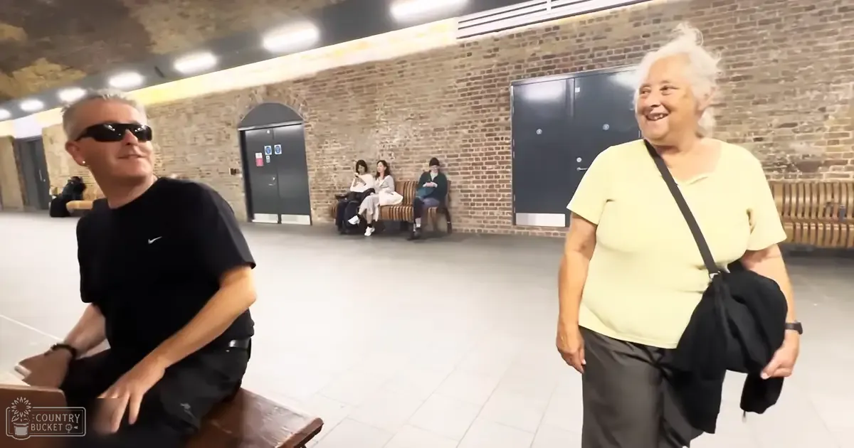 Adult male and older female sitting indoors, brick walls, tiled floor, public space with benches.