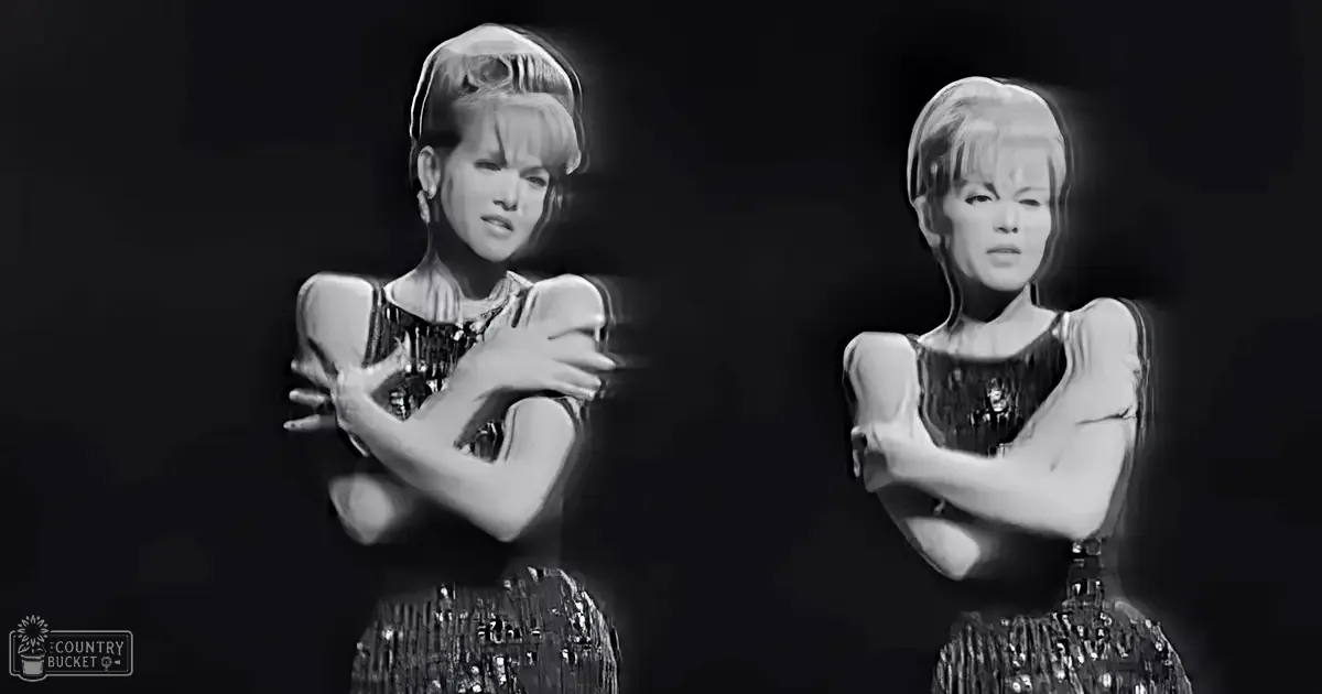 An adult female in a sparkly black dress with short sleeves, wearing a scoop neckline and metallic fabric, stands against an entirely black backdrop.