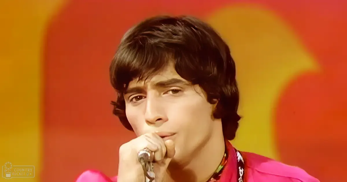 Young adult male wearing a bright pink shirt at what appears to be a music event with stage lighting.
