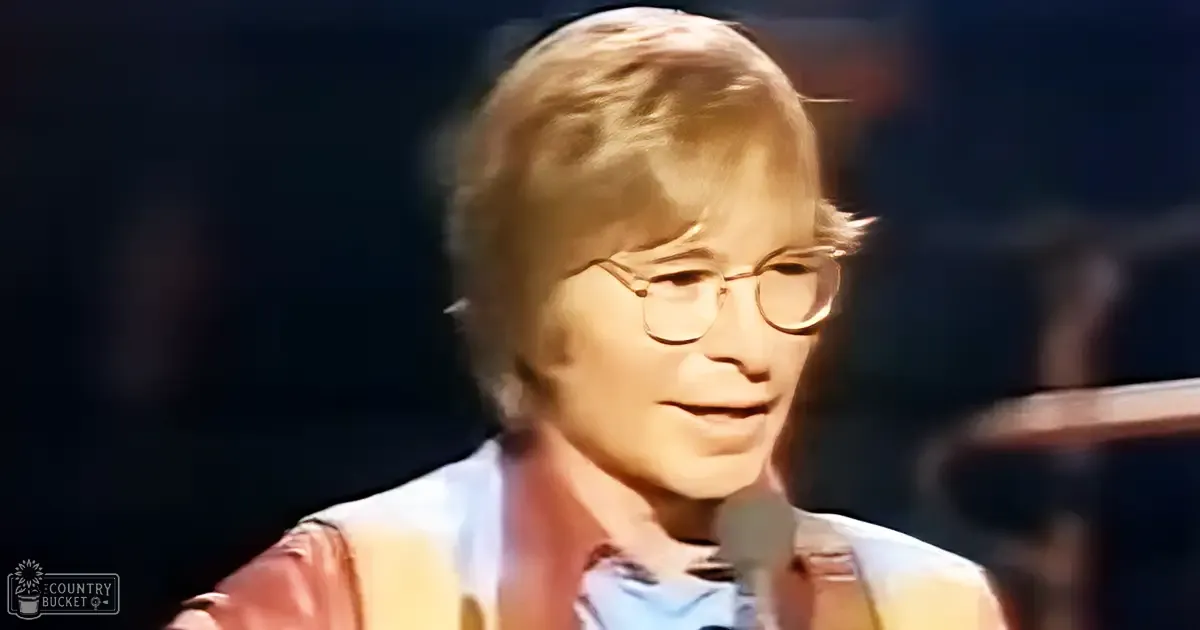 A middle-aged man wearing glasses, a light-colored shirt under a red vest, indoors with stage-like lighting and dark background.