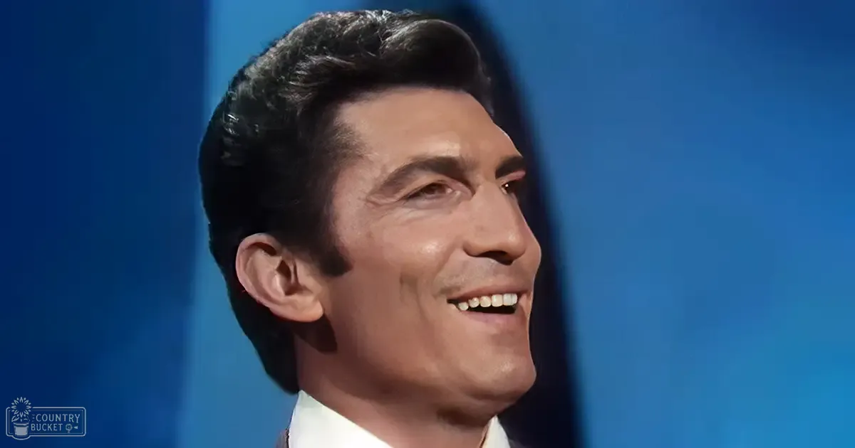 A young adult male in a collared, fitted white shirt against a plain blue indoor background