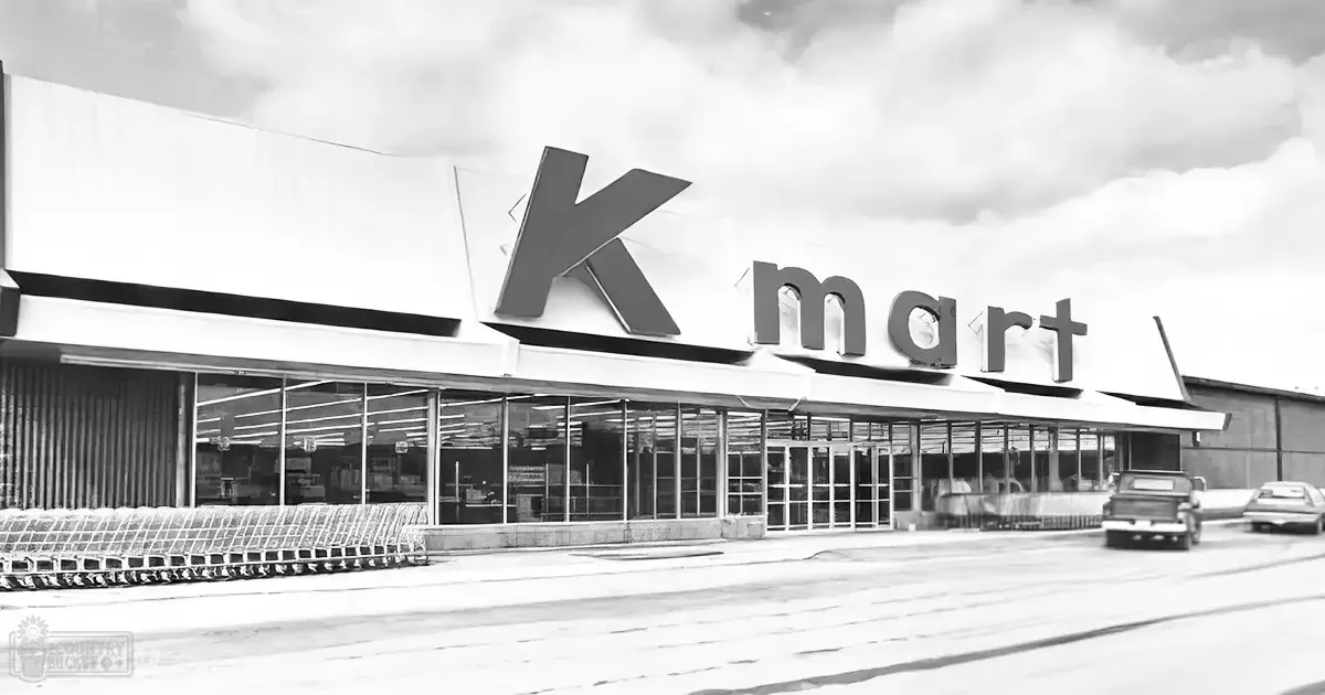 A Kmart store in an urban area with shopping carts outside, a vintage pickup truck parked on the street, and snow on the ground suggesting winter or early spring.