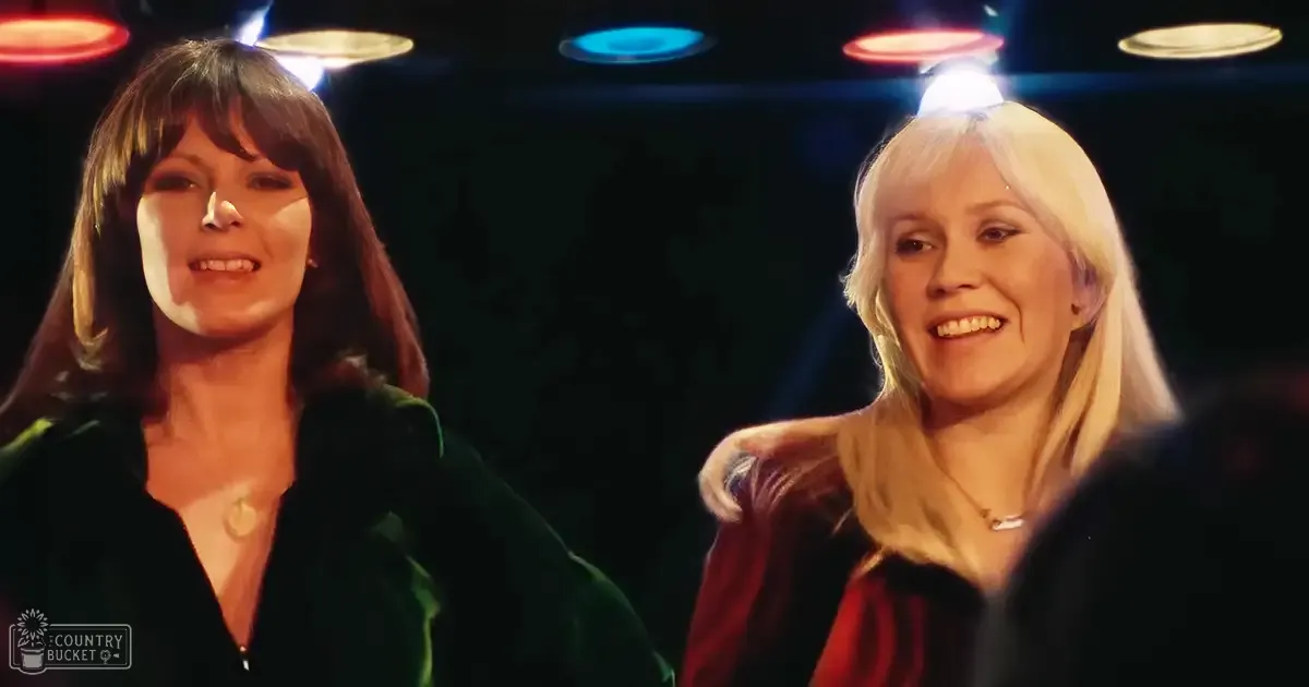 Two women wearing luxurious velvet jackets in a dimly lit indoor setting, possibly a theater or club.