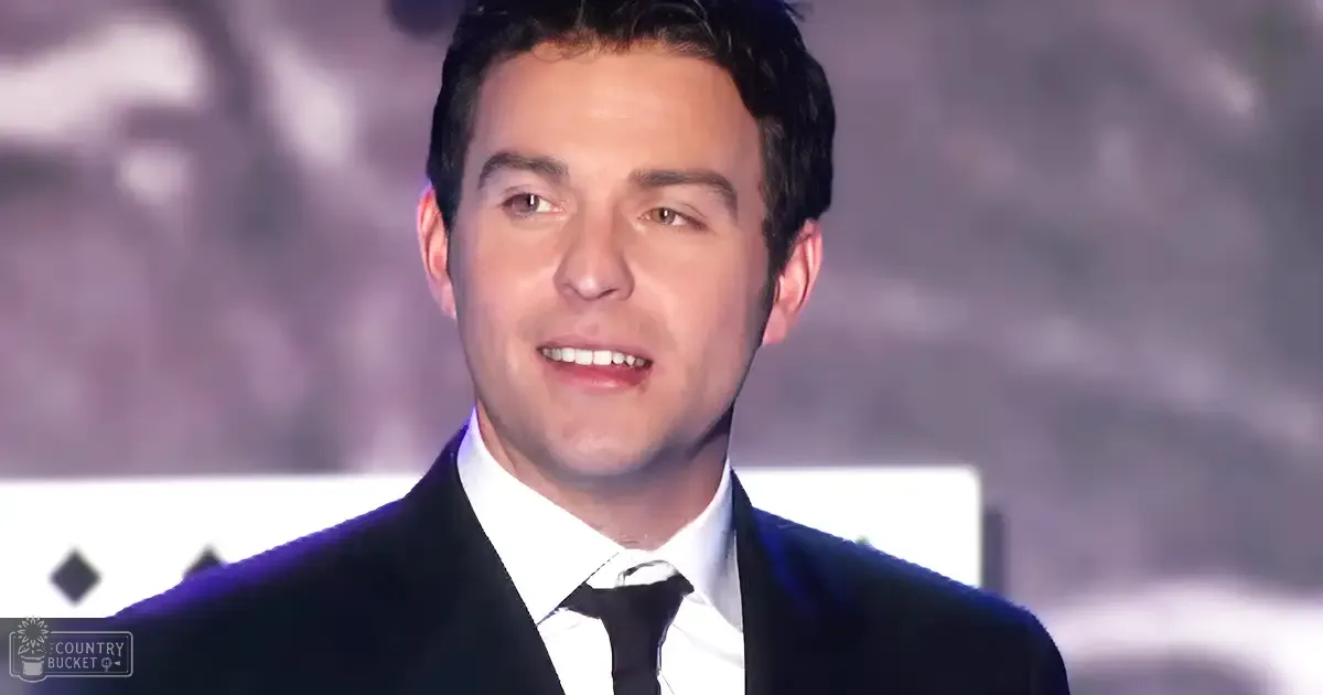 A young adult male in a tailored black suit jacket, white dress shirt, and black tie at an event, possibly a movie premiere.