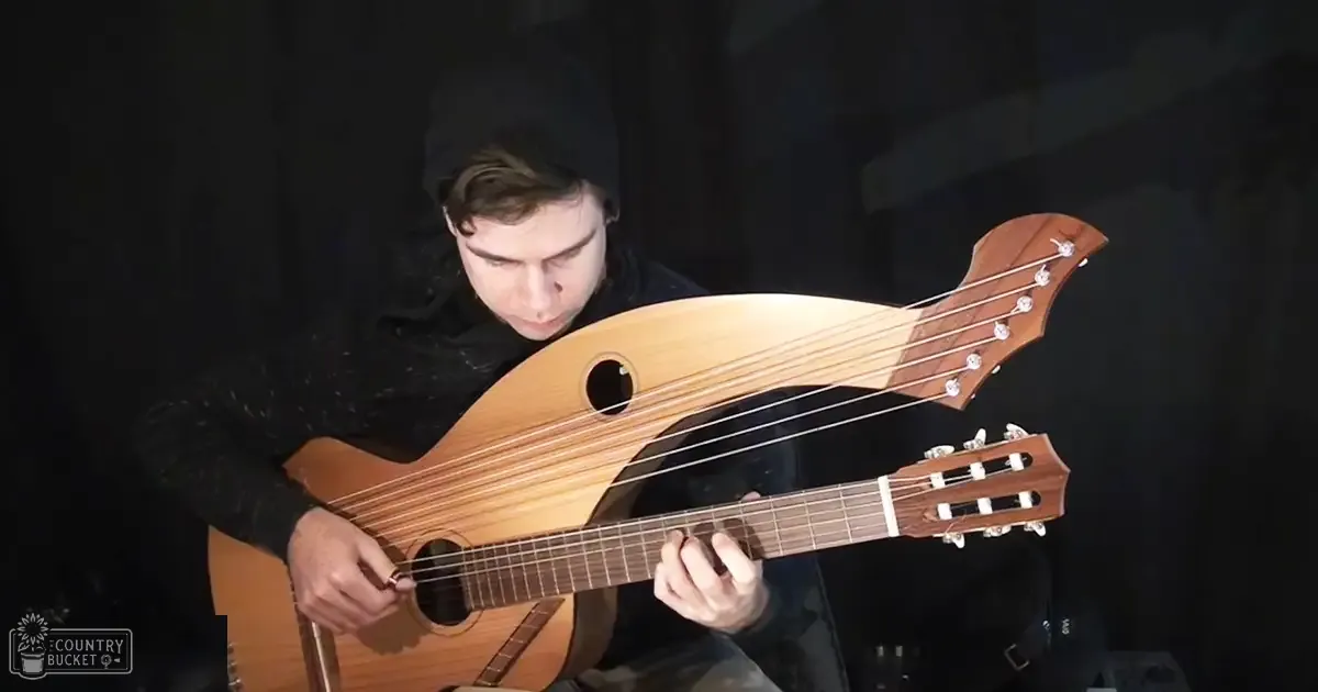A young adult male wearing a textured black long-sleeve garment, dark pants, and a beanie, playing an acoustic guitar in what appears to be a music studio setting.