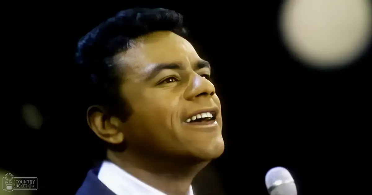 A young adult male in a dark suit jacket and white collared shirt performs on stage under dim lighting.