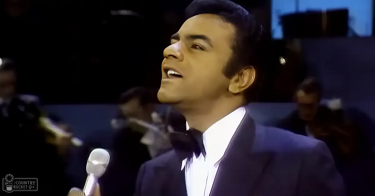 An adult male wearing a dark mid-20th-century formal suit at an indoor event with stage lighting and dim ambient illumination.