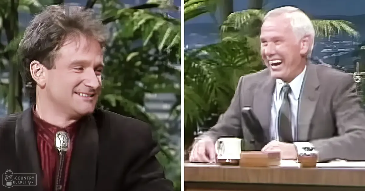 A talk show set with two male hosts, one in a dark blazer and red shirt, the other in a gray suit, against a backdrop mimicking an outdoor tropical setting.
