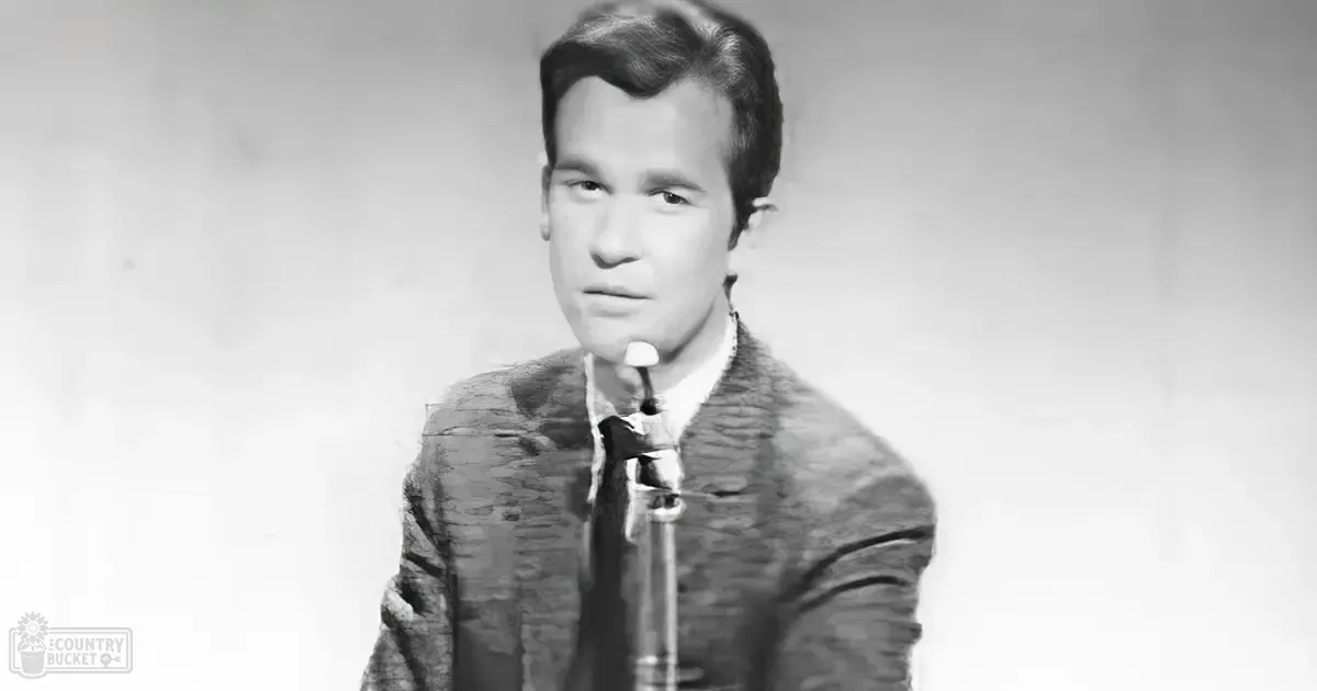 A young adult male in formal attire holding a pipe, standing against a plain white backdrop with minor discoloration.