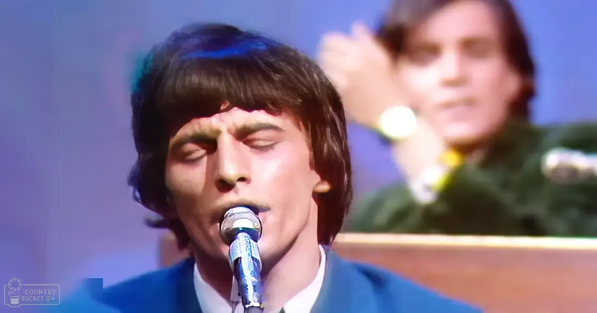 A young adult male in a blue suit jacket sings into a microphone, likely at an event or performance setting.