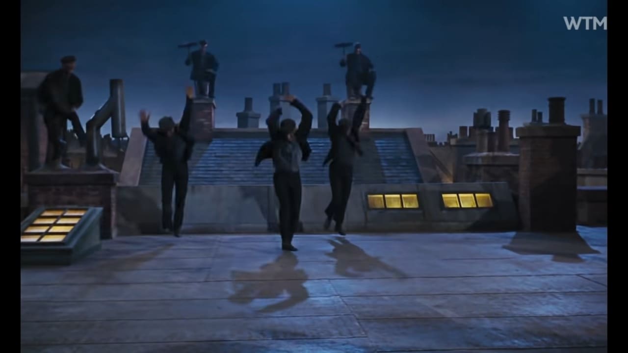 A group of dancers performing on a rooftop at night, surrounded by an urban cityscape with snow visible in the background.