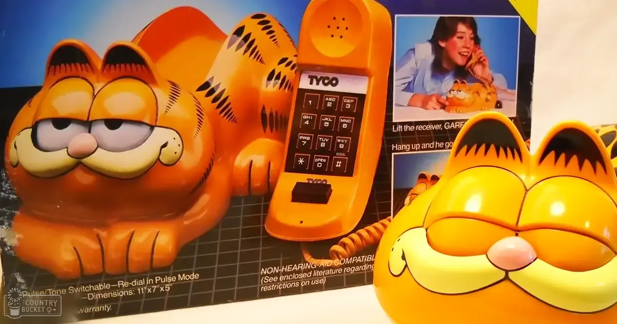A Garfield-themed toy telephone by Tyco displayed with a tabby cat design, text detailing product features, and an adult male holding the phone in a light blue shirt.