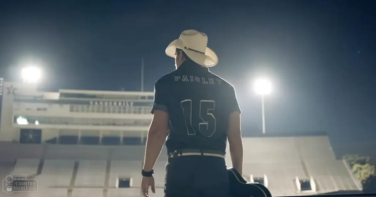 A young adult male wearing a dark-colored, fitted jersey with the number '15' and name 'PAISLEY' stands in an outdoor stadium at night under bright artificial lighting.