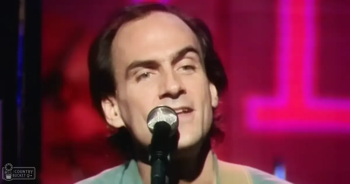 An adult male singer wearing a light green collared shirt with short sleeves on stage at an indoor venue under red and pink lighting.