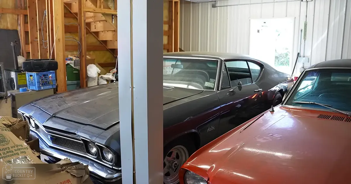 Classic cars in a well-lit indoor garage with wooden framing and insulation.