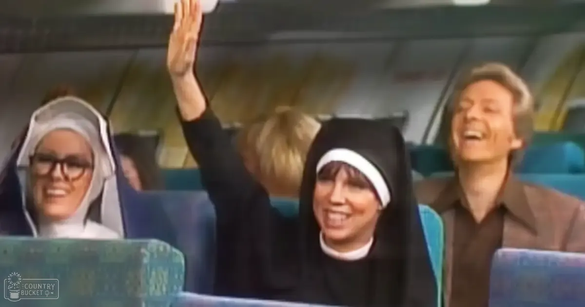 A nun in a black habit with white trim attends an event or gathering, surrounded by other attendees and blue seats.