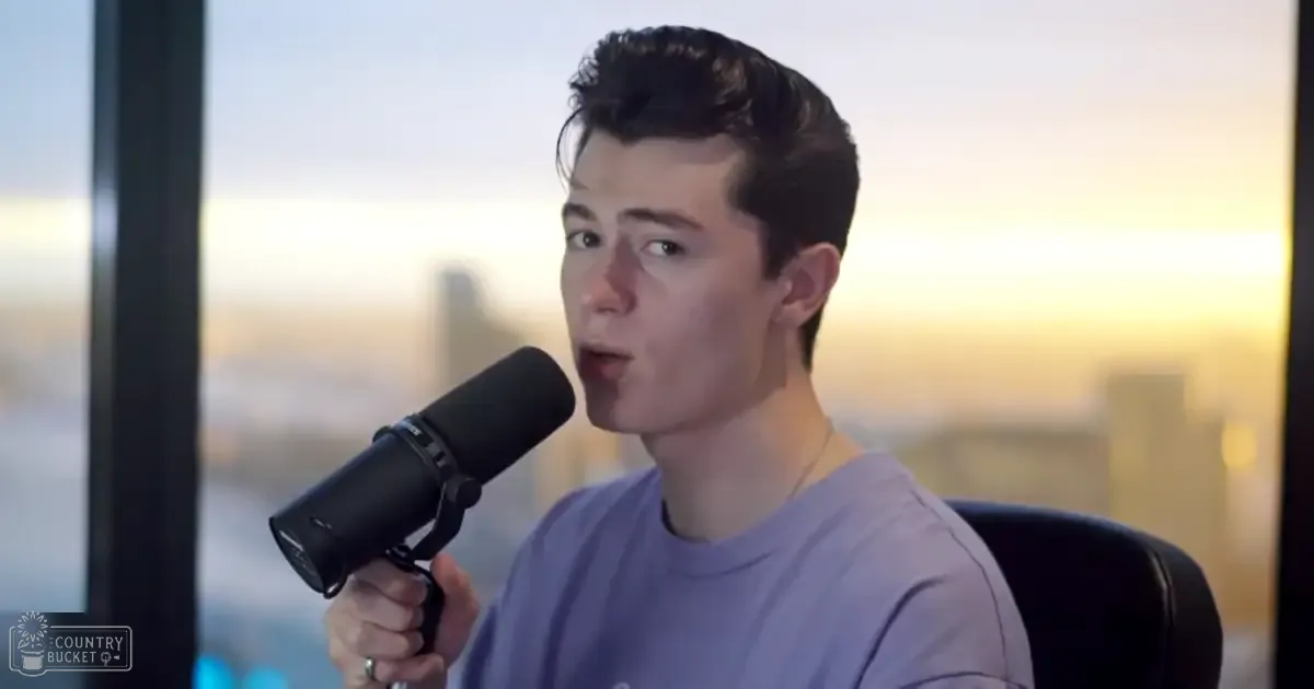 Young adult male holding a black microphone indoors with a cityscape backdrop during golden hour.