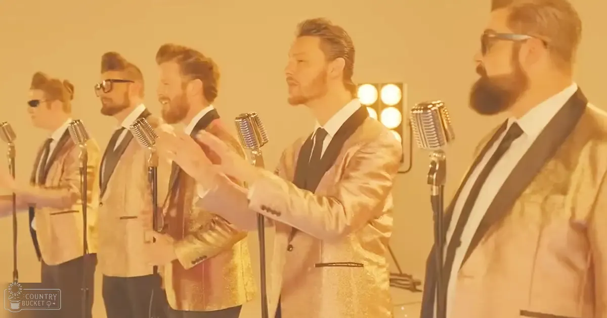 Group of male singers wearing gold jackets and glasses in a recording studio with bright lights creating an orange glow.