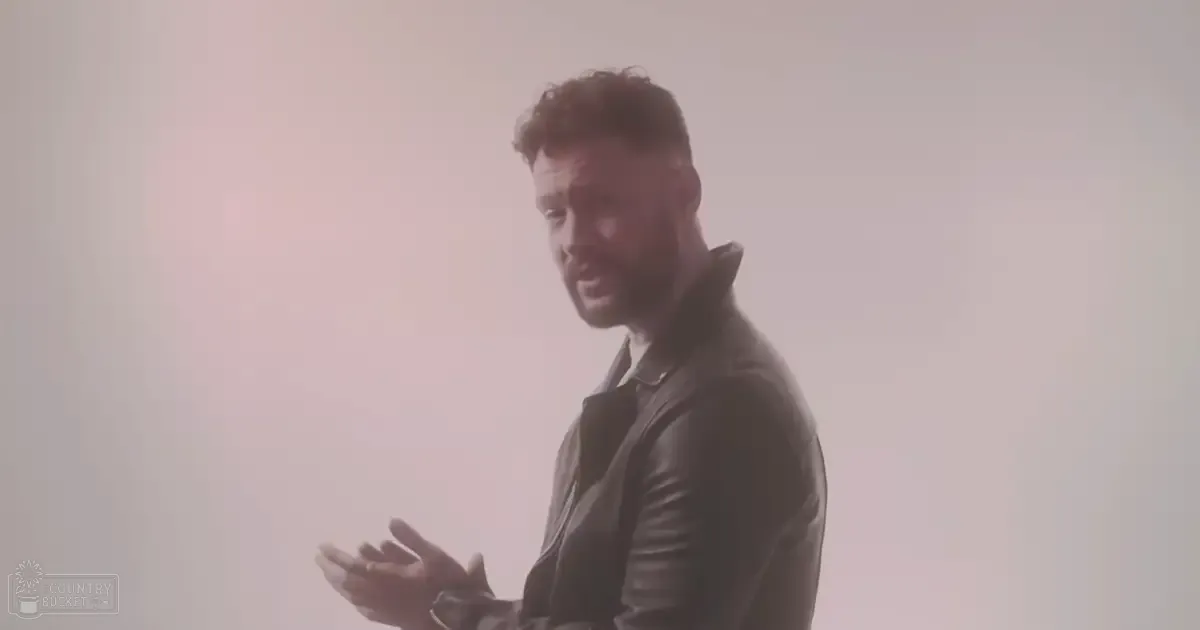 A young adult male wearing a relaxed fit leather jacket indoors with plain light-colored background.