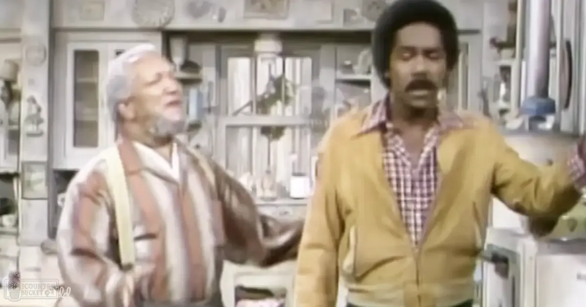 An older adult male in a striped shirt and light jacket stands next to an adult male with dark hair in a yellowish-brown jacket over a checkered red-and-white shirt, set against the backdrop of a well-used indoor kitchen environment.